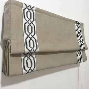 May include: A beige roman shade with a black and white geometric pattern. The shade is raised and the pull cord is visible. The text "TRACK IS COVERED FOR OUTSIDE INSTALL" is visible at the top of the image.