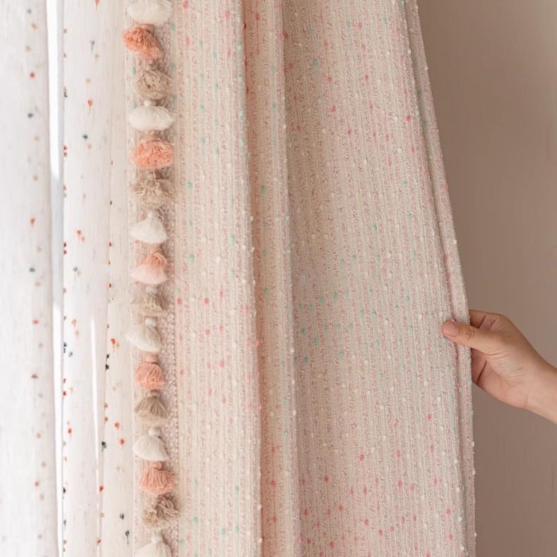 May include: A pair of white curtains with a pink and green speckled pattern. The curtains have a fringe trim with pink and white pom-poms.