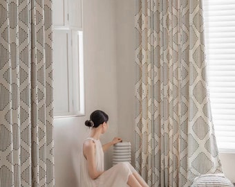 May include: A woman sits on a white rug in a room with white walls and patterned curtains. She is wearing a white dress and is holding a stack of white ceramic plates.