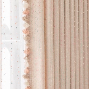 May include: A pair of pink curtains with a white background and small colorful dots. The curtains have a fringe trim with tassels in shades of pink, white, and beige.