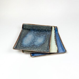 May include: Three ceramic plates stacked on top of each other. The top plate is a dark blue with a light blue glaze. The middle plate is a light blue with a white glaze. The bottom plate is a dark blue with a light blue glaze.