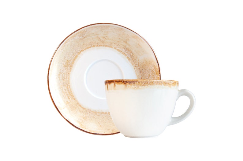 May include: A white ceramic coffee cup and saucer with a brown and beige glaze. The cup has a rounded shape and a handle. The saucer has a slightly raised rim.