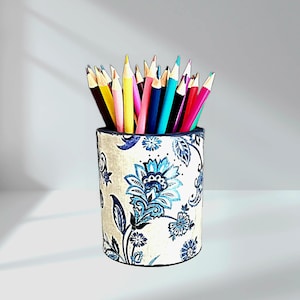 May include: A cylindrical pencil holder with a cream-colored background and a blue floral pattern. The holder is filled with a variety of colored pencils, including yellow, pink, blue, and red. The pencils are sharpened and ready for use.