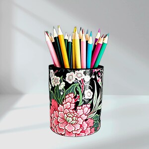 May include: A black pencil holder with a floral design featuring pink, white, and green flowers. The holder is filled with colored pencils.