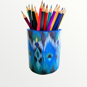 May include: A blue and green patterned ceramic pencil holder with a variety of colored pencils sticking out of the top.