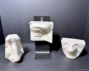 May include: Three off-white sculptural plaster casts featuring anatomical facial details. One piece depicts an eye, one a nose, and one a mouth. The eye sculpture is mounted on a black metal stand, while the nose and mouth pieces are free-standing.