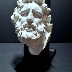 Puede incluir: Una escultura de yeso blanco de un rostro barbudo con ojos cerrados y cabello ondulado, montada sobre un soporte rectangular negro. La escultura presenta rasgos faciales detallados y rizos texturizados. El texto fromthemold.art es visible abajo.