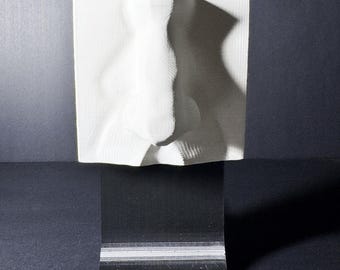 May include: A white, three-dimensional square plaque featuring a sculpted human nose in the center. The plaque is mounted on a black, curved stand and includes a small metal ring at the top. The text fromthemold.art is visible at the bottom.