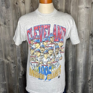 May include: A gray t-shirt with a graphic of the 1995 Cleveland Indians baseball team. The graphic features the team's logo and the text "1995 Division Champs".