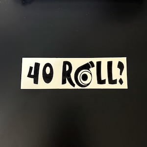 May include: A rectangular sticker with the text "40 ROLL?" in black, featuring a stylized turbocharger graphic. The sticker is on a black background.