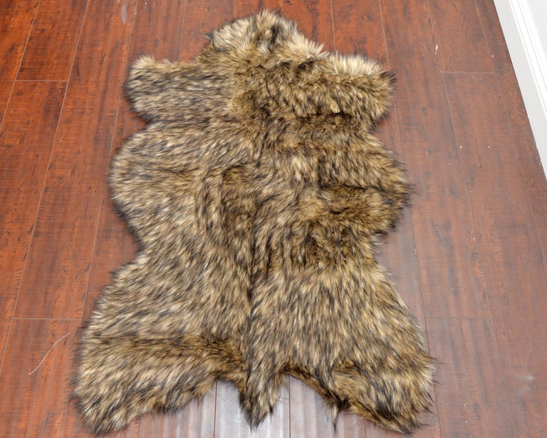 May include: A brown and black faux fur rug with a shaggy texture. The rug is laid out flat on a wooden floor.