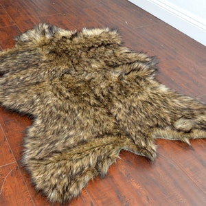 May include: A brown and black faux fur rug with long, shaggy fibers. The rug is laid out flat on a wooden floor.