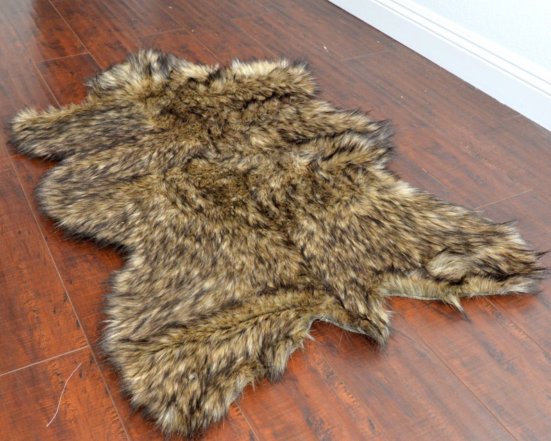 May include: A brown and black faux fur rug with long, shaggy fibers. The rug is laid out flat on a wooden floor.