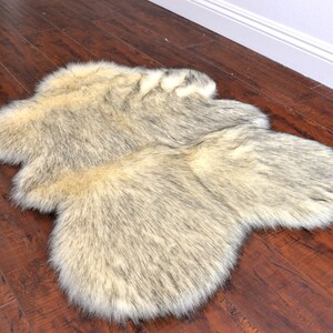 May include: A fluffy faux fur rug in shades of beige and gray. The rug has a long, soft pile and is perfect for adding a touch of warmth and luxury to any room.