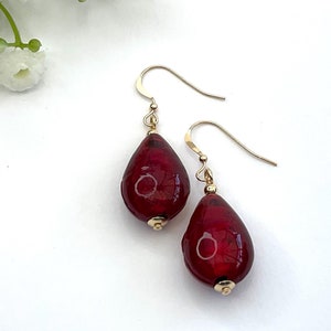 May include: A pair of dangle earrings with red teardrop-shaped glass beads and gold hooks.