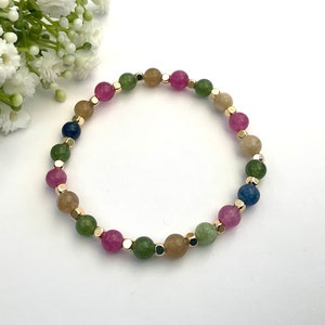 May include: A multi-colored beaded bracelet with gold accents. The bracelet features pink, green, blue, and brown beads.