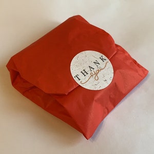 May include: A red tissue paper gift bag with a round white sticker that says "THANK you" in black text.