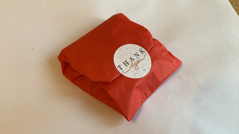 May include: A red tissue paper gift bag with a round white sticker that says "THANK you" in black text.