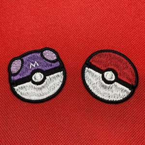 Könnte beinhalten: Zwei gestickte Bügelbilder mit dem Pokemon Pokeball-Design. Ein Patch ist lila und weiß mit dem Buchstaben "M" in der Mitte. Der andere Patch ist rot und weiß.