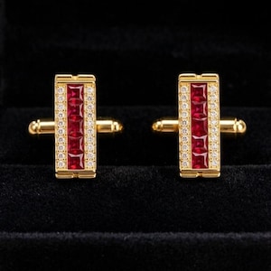 Puede incluir: Un par de gemelos rectangulares de oro con una fila central vertical de cuatro rubíes de color rojo intenso tallados en forma cuadrada, flanqueados por dos filas delgadas de pequeñas piedras blancas redondas en un marco dorado.