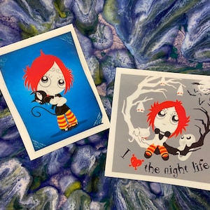 May include: Two illustrated cards featuring a red-haired girl with a black cat and a black bow tie. The first card has a blue background and the girl is holding the cat. The second card has a gray background and the girl is standing in front of a tree with a white cat and a ghost. The text on the second card reads "I ♥ the night life".