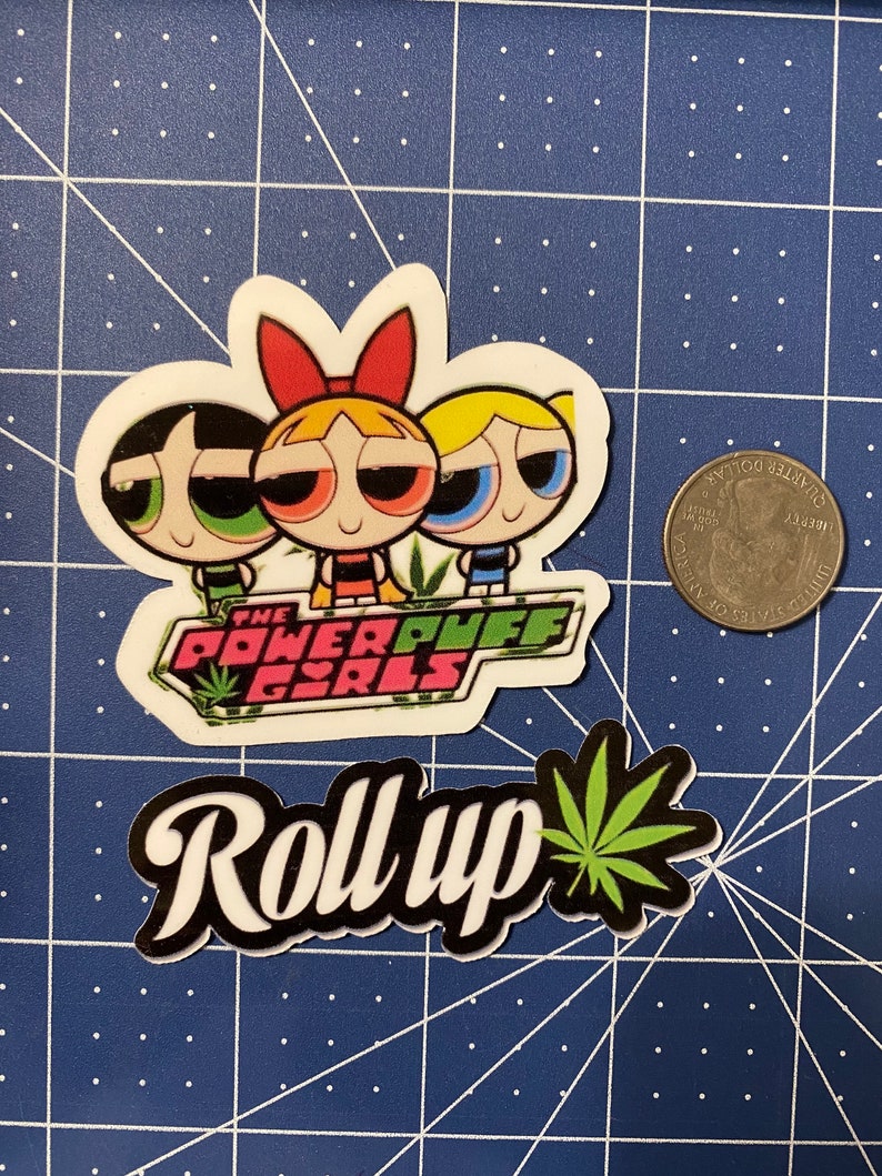 May include: A sticker featuring the Powerpuff Girls cartoon characters with the text "The Powerpuff Girls" and a green marijuana leaf. Below the sticker is a black and white sticker with the text "Roll Up" and a green marijuana leaf.