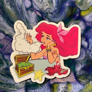 May include: A sticker featuring a cartoon mermaid with pink hair, wearing a seashell bra and holding a joint. She is surrounded by smoke and a treasure chest filled with green items. A red crab and a yellow starfish are also included in the design.