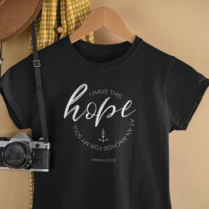 May include: Black t-shirt with a white circle graphic that says "I have this hope as an anchor for my soul" with an anchor symbol and the text "Hebrews 6:19".