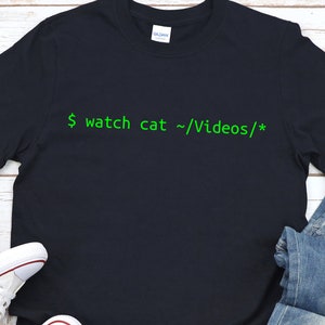 May include: A black t-shirt with green text that reads "$ watch cat ~/Videos/*"