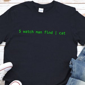 May include: A dark blue t-shirt with green text that reads "$ watch man find | cat".