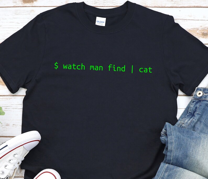 May include: A dark blue t-shirt with green text that reads "$ watch man find | cat".