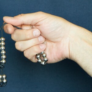 May include: A silver beaded necklace with black string. The beads are round and have a smooth finish. The necklace is knotted at the ends.