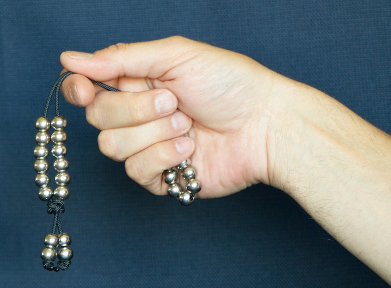 May include: A silver beaded necklace with black string. The beads are round and have a smooth finish. The necklace is knotted at the ends.