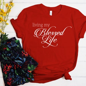 Op de afbeelding: Rood T-shirt met witte tekst die "living my Blessed Life" luidt.