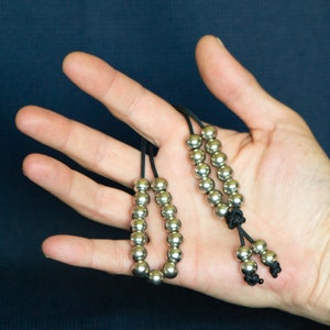 May include: Two silver beaded necklaces with black cords. The necklaces are on a hand with the cords tied together at the bottom.