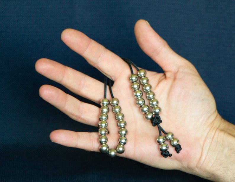 May include: Two silver beaded necklaces with black cords. The necklaces are on a hand with the cords tied together at the bottom.