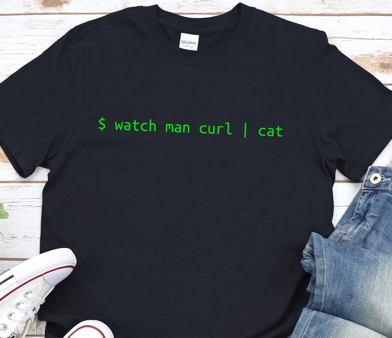 May include: A dark blue t-shirt with the text "$ watch man curl | cat" printed in green.