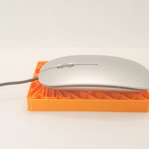 May include: A silver computer mouse sits on an orange mousepad with a geometric pattern. The mouse has a modern design and a scroll wheel. A grey cable extends from the mouse. The rectangular mousepad is made of plastic.