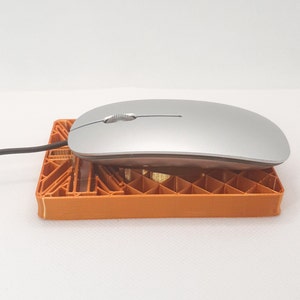May include: A silver wireless computer mouse resting on an orange plastic stand. The mouse has a single button and a scroll wheel.