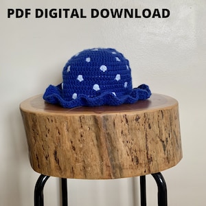 May include: Blue crochet sun hat with white polka dots. The hat has a wide brim and a ruffled edge. The hat is sitting on a wooden stool.