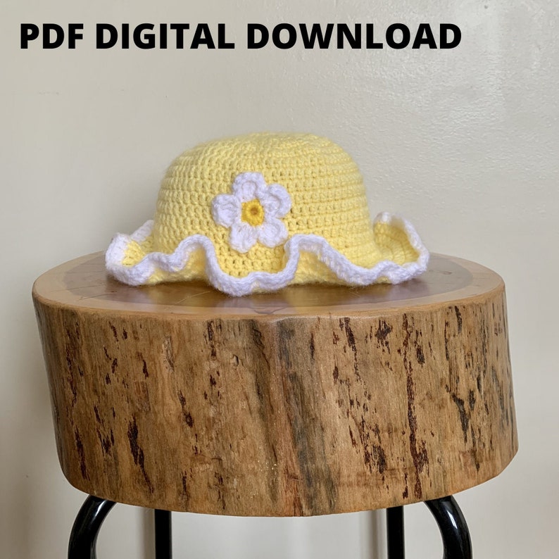 May include: A yellow crochet sun hat with a white crocheted flower on top. The hat is sitting on a wooden stool.