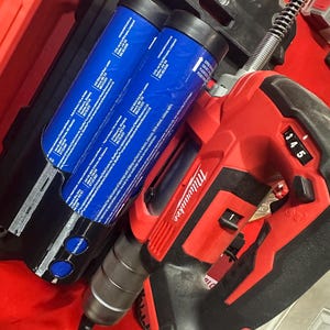 Puede incluir: Un taladro Milwaukee rojo y negro y una caja Packout negra con dos contenedores cil&iacute;ndricos azules. El taladro tiene una pantalla digital que muestra el n&uacute;mero 345. La caja Packout tiene el logotipo de Milwaukee.