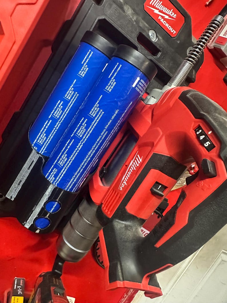 Puede incluir: Un taladro Milwaukee rojo y negro y una caja Packout negra con dos contenedores cil&iacute;ndricos azules. El taladro tiene una pantalla digital que muestra el n&uacute;mero 345. La caja Packout tiene el logotipo de Milwaukee.