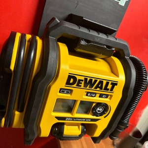 Peut inclure: Un compresseur d'air DeWalt jaune et noir de 20 V au lithium-ion avec un tuyau noir et un écran numérique. Le compresseur est monté sur un support mural noir.