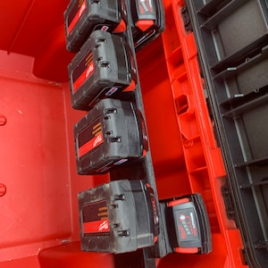 May include: A red toolbox with a black organiser insert holding four black and red power tool batteries. The batteries are labelled "Milwaukee"