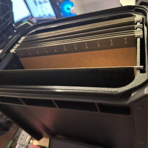 May include: Black, open, hard-shell case containing several hanging file folders. The case is made of a durable material and has a handle. The file folders are tan and have metal tabs. The case is for document storage.