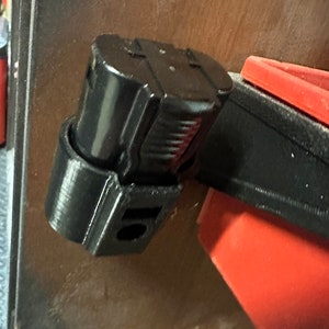 May include: A black 3D printed battery holder for a power tool battery. The holder is attached to a red and black tool organiser.