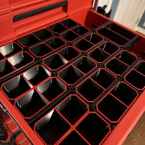 May include: A red Milwaukee Packout toolbox with a drawer open, revealing a black organiser with multiple compartments. The organiser is designed to hold small tools and accessories.