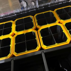 May include: A black and yellow organizer with multiple compartments. The organizer has a clear lid and is designed to hold small items. The compartments are yellow with black interiors, providing a structured storage solution.