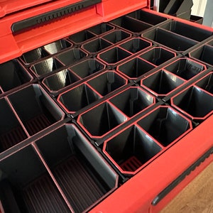 Peut inclure: Un tiroir de boîte à outils rouge avec des séparateurs noirs. Les séparateurs créent de multiples compartiments pour organiser de petits objets.